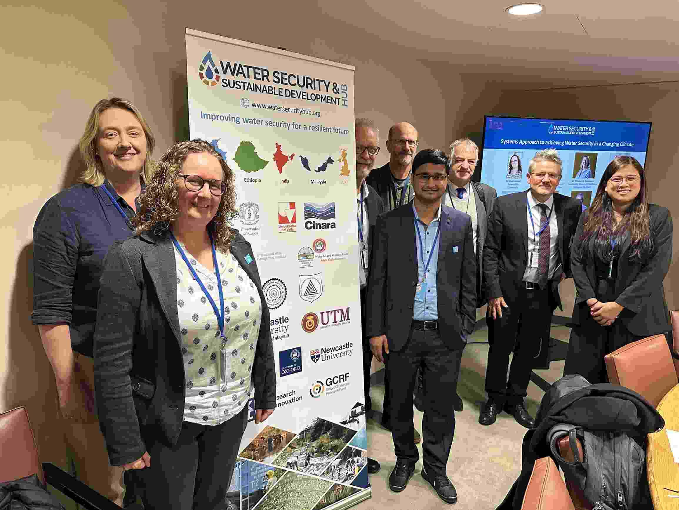 A mixed group of Hub researchers smile and stand together around a Water Security Hub banner 